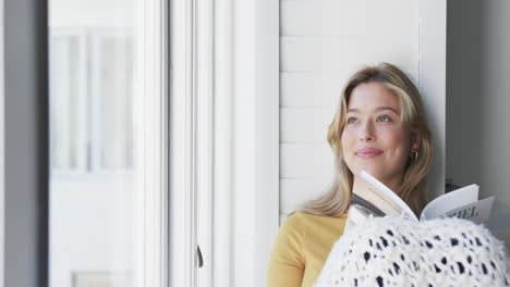 Happy-biracial-woman-sitting-next-to-window-reading-book-at-home,-slow-motion