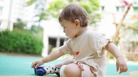 asian toddler girl sitting on the playground and putting things in her mouth - concept: learning, motor skills, taste ,trying, growing, development