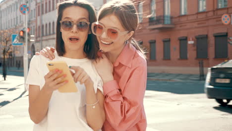 two young women friends looking at a phone on a city street