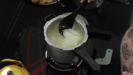 a mother is cooking delicious indian dish in the kitchen by stirring the food and adding ingredients