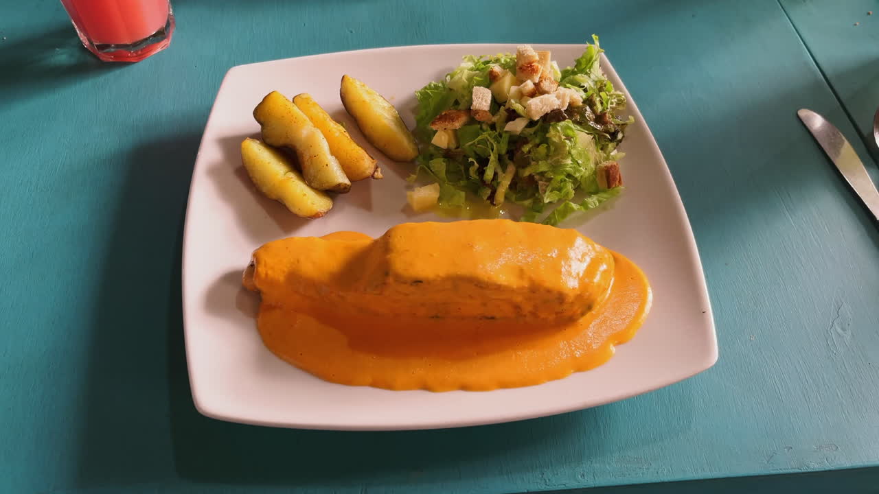 Plated salmon covered in creamy orange sauce, with salad and wedges
