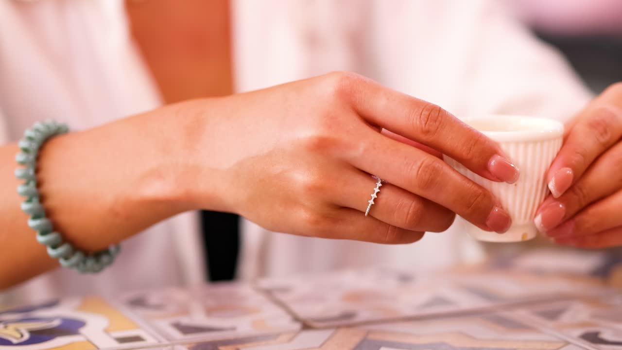 Close-up of hands with a bracelet gently holding a ribbed tea cup over a patterned surface.