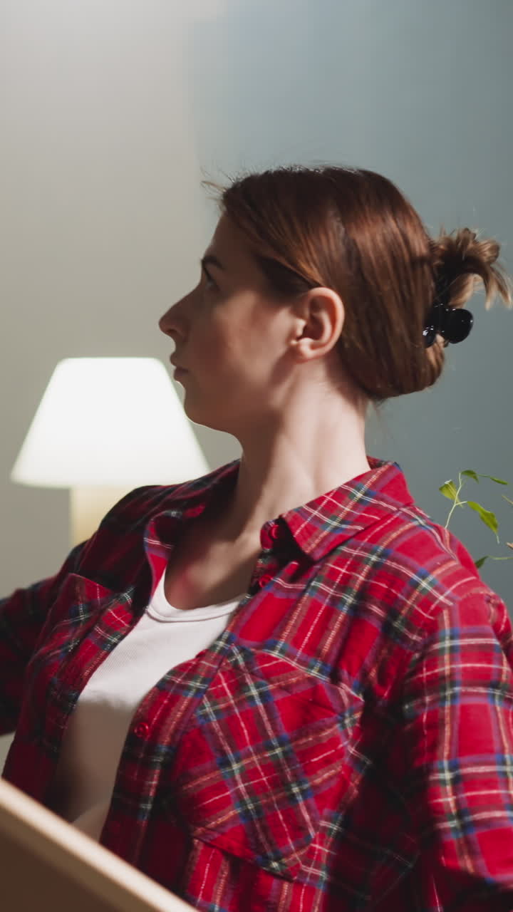 Lady chooses special painting to hang on brick wall in renovated room side view. Woman decorates new apartment. Interior design and contemporary trends