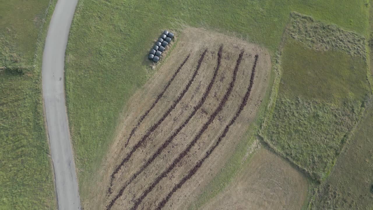 Aerial view with a drone over coastal farmland in Cantabria showing lines of seaweed fertilizer, contrasting green fields, a rural road and round bales of hay wrapped in black plastic
