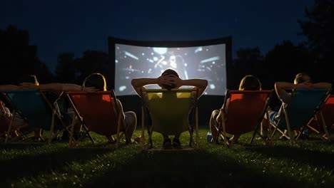 a group of friends enjoying an outdoor movie night under the stars, relaxing on colorful chairs in front of a large screen displaying a film