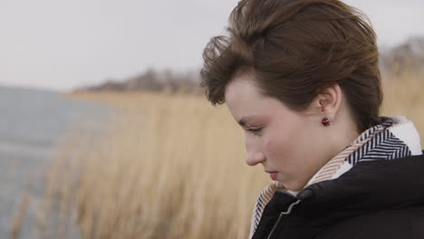 Close-Up-View-Of-Teenage-Girl-With-Short-Hair-Wearing-Scarf-And-Coat-Looking-At-The-Sea-On-A-Windy-Day,-Then-She-Looks-At-Camera