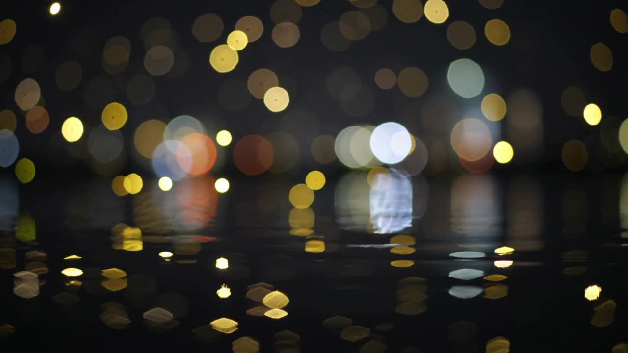 Luci del porto sfocate e tremolanti e riflessi che si muovono sul lungomare di notte, a causa della brezza.