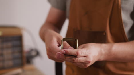 master puts large metal buckle onto leather belt in workshop