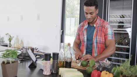 hombre biracial preparando comida, usando tableta y cortando verduras en una cocina moderna, en cámara lenta