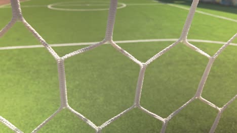 slide shot behind empty football goal net on synthetic grass pitch