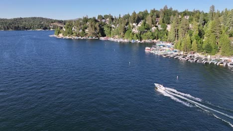 Siguiendo-Una-Lancha-Rápida-En-El-Lago-De-Punta-De-Flecha-De-California-Con-Una-Vista-De-Las-Casas-Y-Los-Muelles-Junto-Al-Lago-Día-Soleado-Pan-De-Camiones-Aéreos