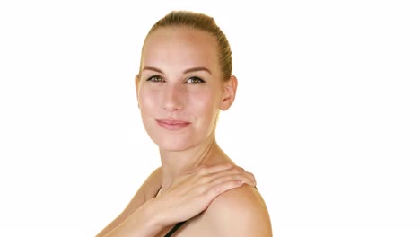 beautiful young woman on seamless white studio background holding shoulder in a black bra staring intently into the camera with her hazel eyes and pulled back hair while slowing zooming out