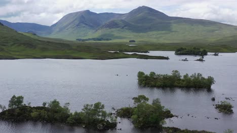 Islas-Boscosas-En-El-Lago-Con-Montañas,-Rannoch-Moor,-Tierras-Altas,-Escocia,-Ancho,-Aéreo