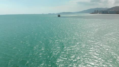 Fly-towards-a-boat-in-green-oceans-with-beautiful-mountains-in-the-background