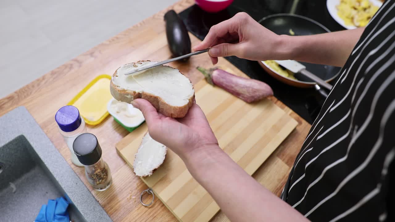 Hands spreading cream cheese or butter on a slice of bread for breakfast