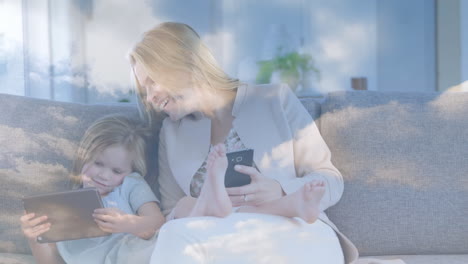 animation of clouds on sky over happy caucasian mother with daughter using tablet and smartphone