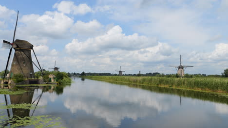 Wunderschöne-Aufnahme-Mehrerer-Windmühlen-Mit-Spiegelungen-Im-Wasser-Und-In-Einer-Typisch-Holländischen-Landschaft