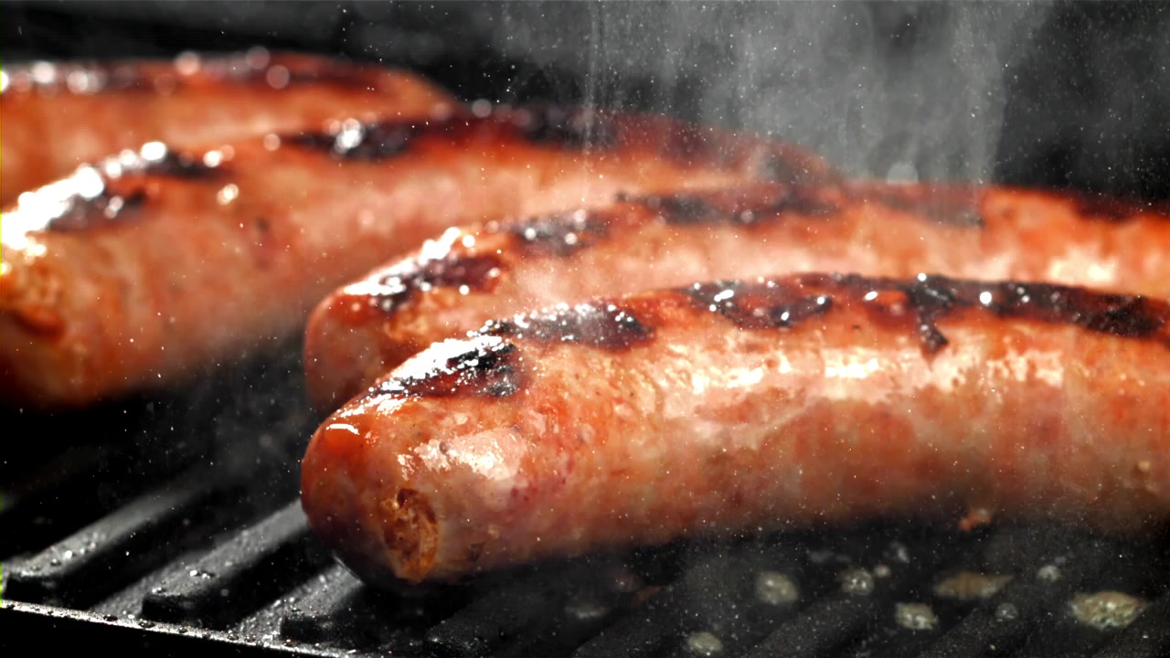 Salsicce deliziose che cuociono su una griglia per barbecue con fumo