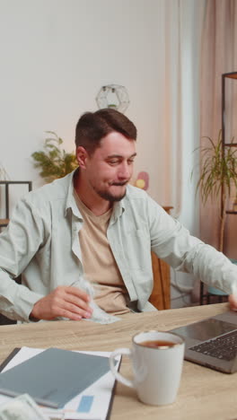 successful young man freelancer using laptop celebrate success falling money at home office table
