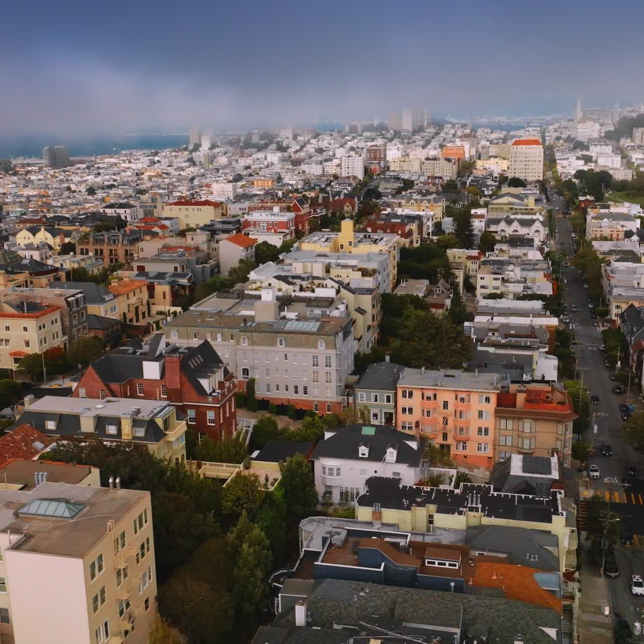 Drone rising over the beautiful urban architecture at daytime. Lively bright San Francisco at the backdrop of blue foggy sky