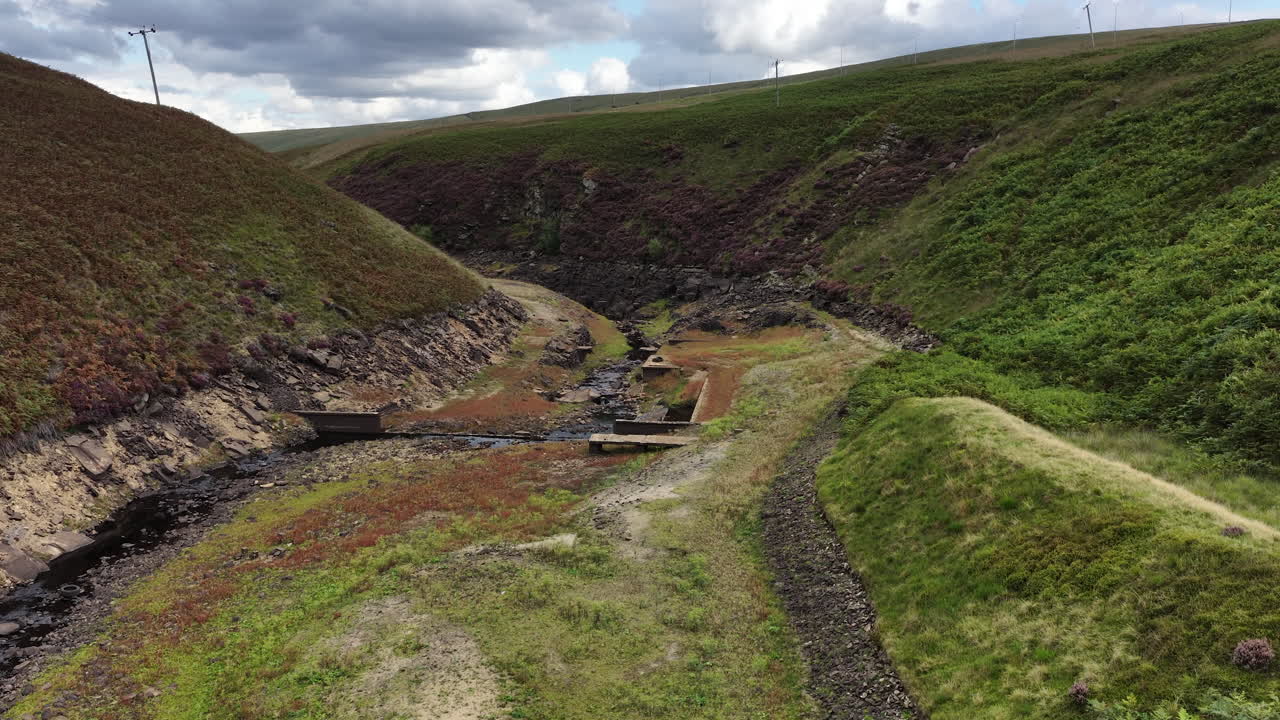 Drone flying through a green valley near Booth Wood Reservoir in Ripponden, showcasing hillside slopes, a flowing stream, and Yorkshire countryside scenery