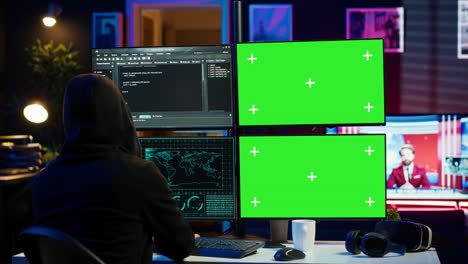 hooded man writing lines of code on green screen pc from apartment