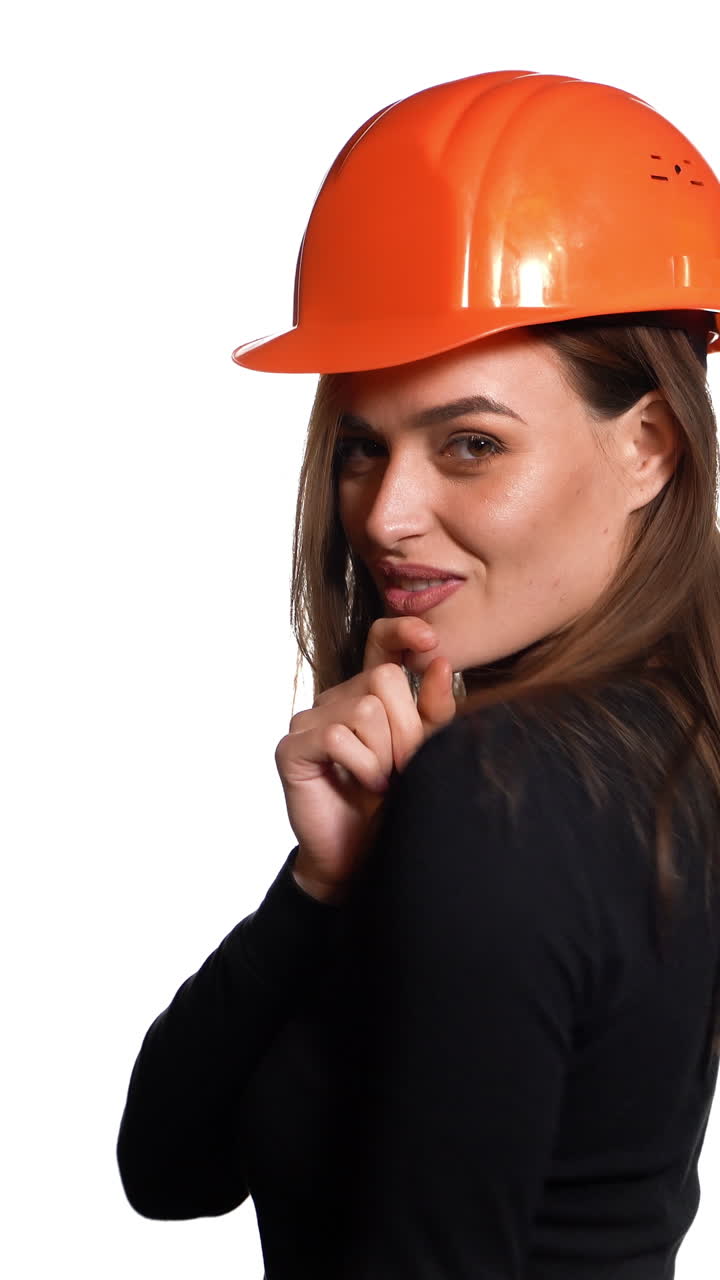Beautiful woman in orange helmet and black golf is poses for the camera on a white background in the studio. Vertical video
