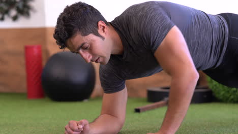 entrenador muscular haciendo variaciones de ejercicio de tablones en el suelo de hierba del gimnasio