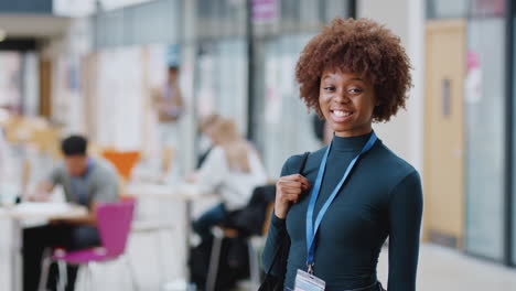 Portrait-Of-Smiling-Female-College-Student-In-Busy-Communal-Campus-Building