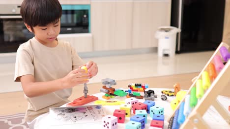 A young boy assembles colorful blocks on a table in a well-lit room, showcasing creativity and concentration