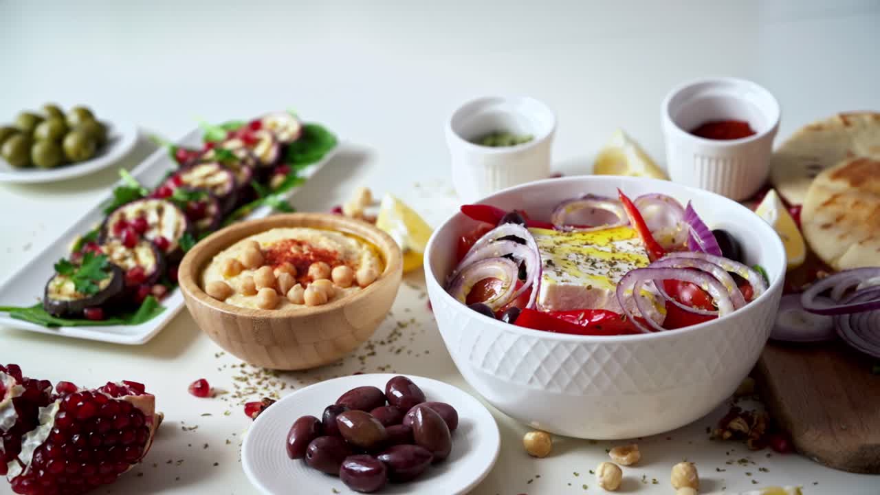 Close-up view of a table full of healthy national food in dishes. Sliced vegetables, salads and appetizers. A man filling the salad with olive oil. Slow motion