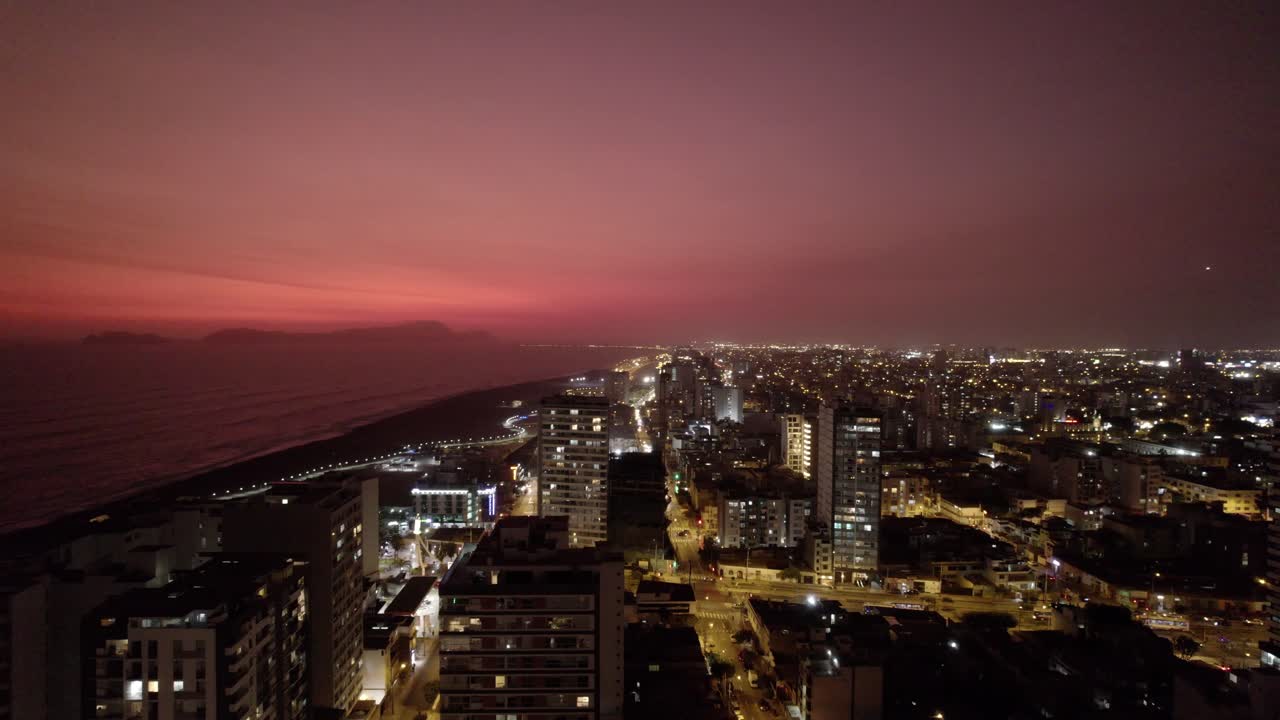 Vista aérea panorámica de una ciudad costera al atardecer con cielo rojo.