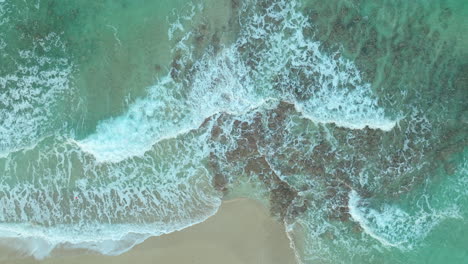 Shoreline-in-Cyprus---Emerald-Crystal-Clear-Sea-Water-Waves-with-Foam-Rolling-in-Slow-Motion-Over-Golden-Sandy-Beach---aerial-top-down-descending