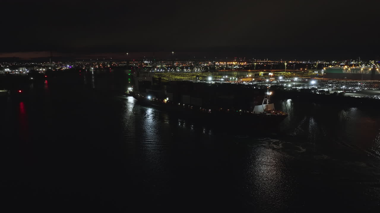 avión no tripulado de noche volando sobre el agua con un barco de contenedores de envío que sale del río yarra de newport