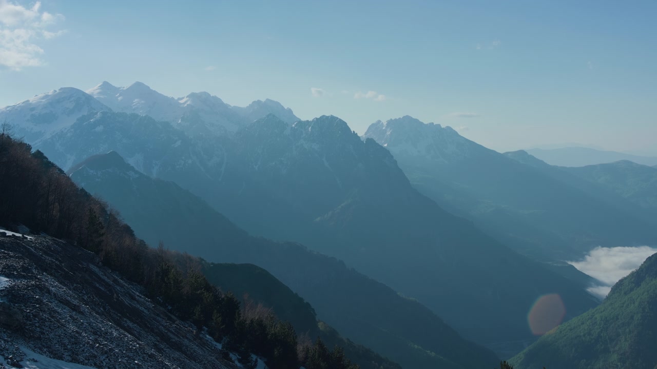 Lembah gunung bersalju, pohon hijau, dan puncak berbatu, pemandangan dari tripod statis. Pemandangan pegunungan Alpen musim dingin dengan hutan di bawah langit biru cerah