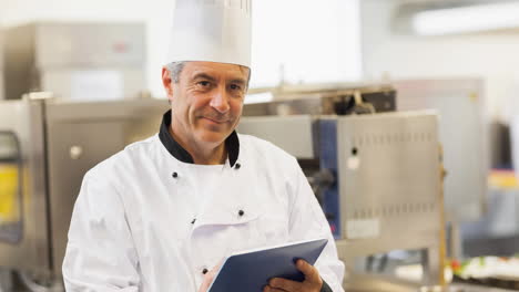 un chef caucásico sonriente con un delantal usando una tableta en una cocina profesional
