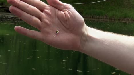 a man holds a fish hook, poised over the water - close up