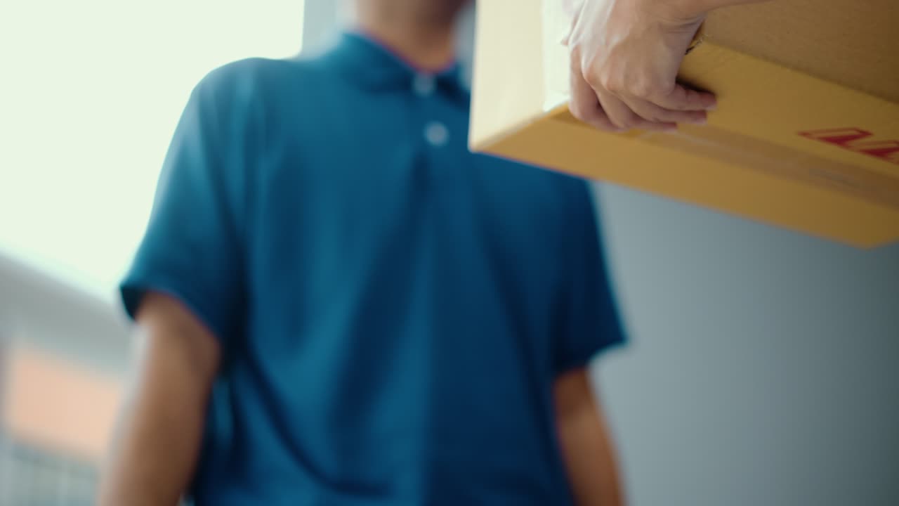 cerrar el paquete en la mano del hombre de entrega de uniforme azul al cliente frente a la casa de las compras en línea con buen servicio. mensajero hombre entregando un paquete postal de caja de cartón a destino.