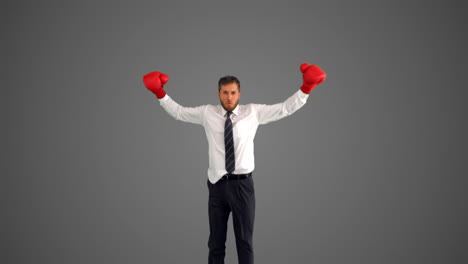 hombre de negocios con guantes de boxeo saltando y golpeando sus puños sobre un fondo gris