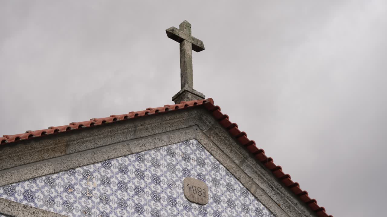 exterior of old chapel with tiled facade cross and engraved 1883 stone on cloudy day