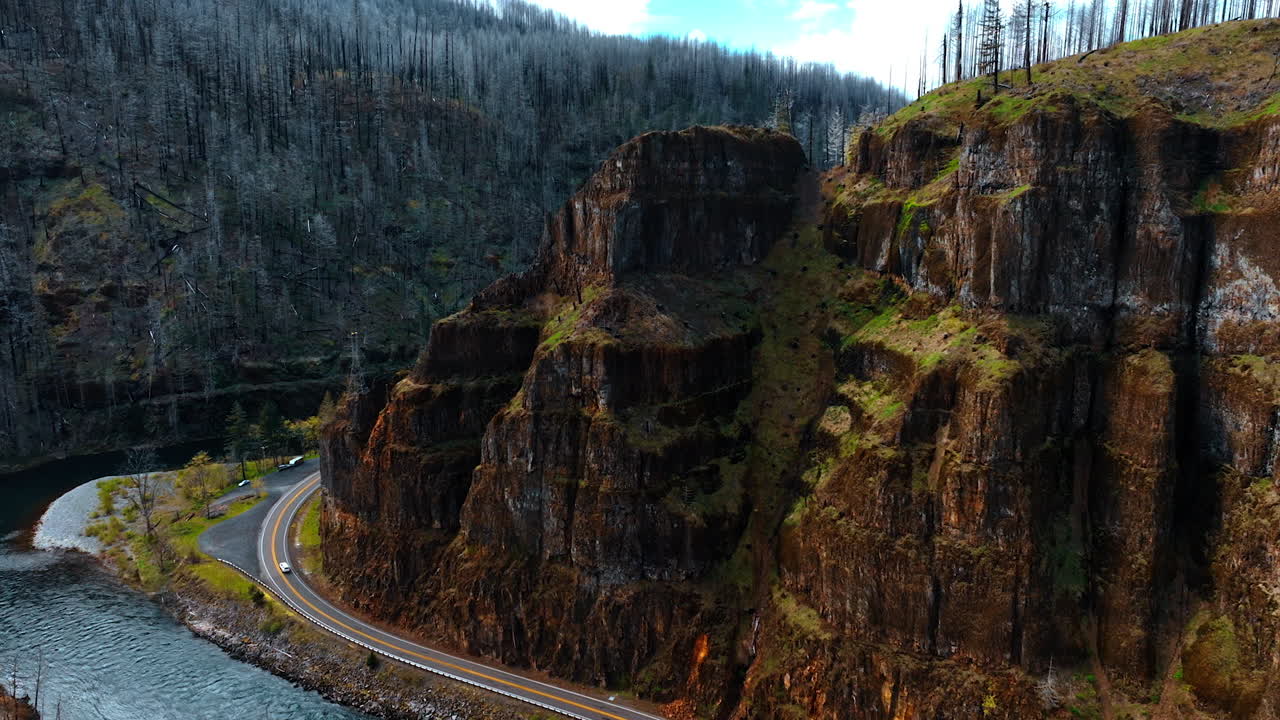 Stunning steep rocks in the Oregon State at daytime. Highway with moving car goes around the mountain. Dry pine trees covering the mountains. Top view.