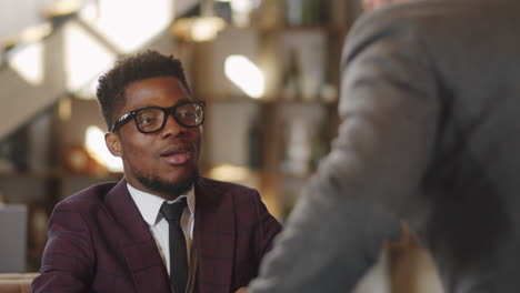 black businessman shaking hands and speaking with colleague in restaurant