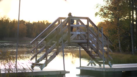 young hiking boy walking on wooden bridge over beautiful lake, beautiful autumn scenery at sunset