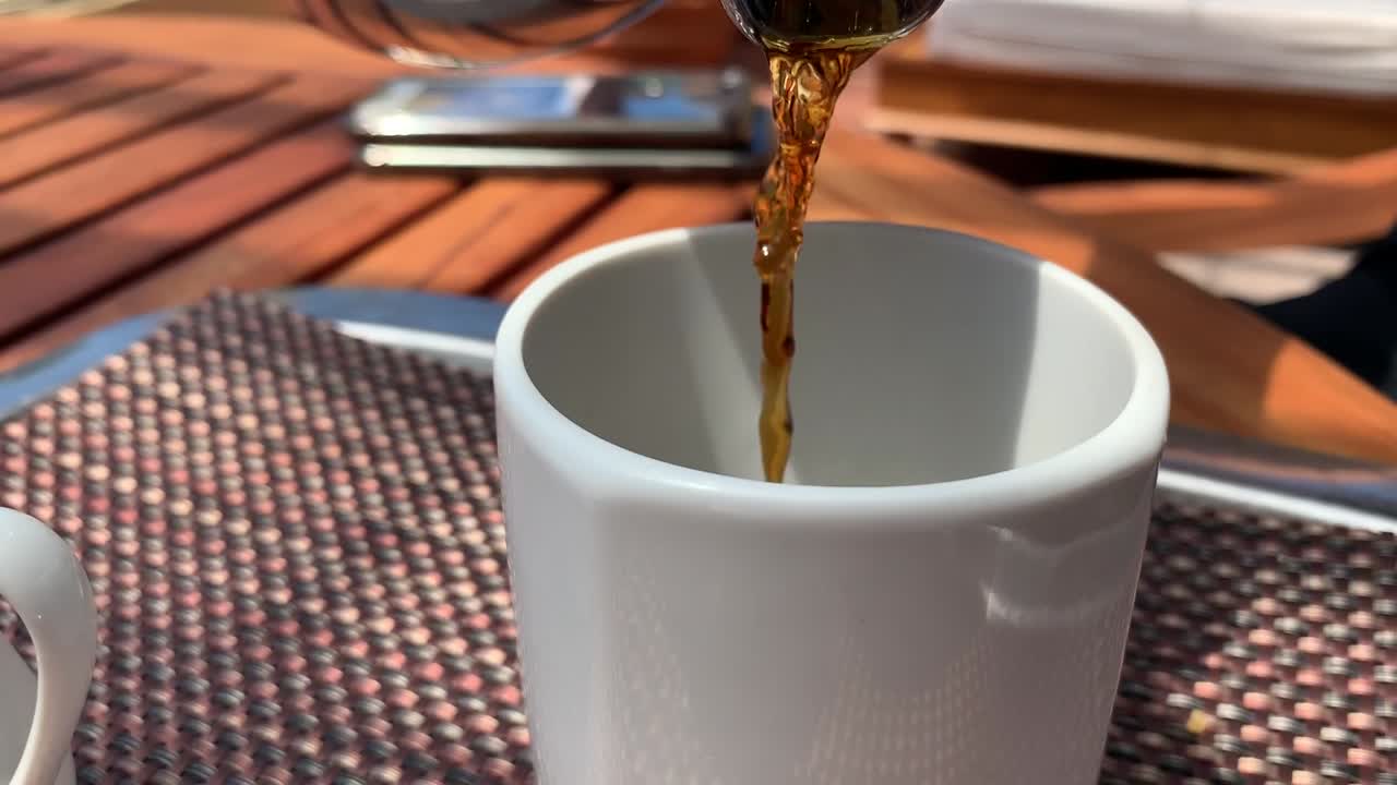 un primer plano de café caliente que se vierte en una taza blanca al aire libre en una terraza en la azotea
