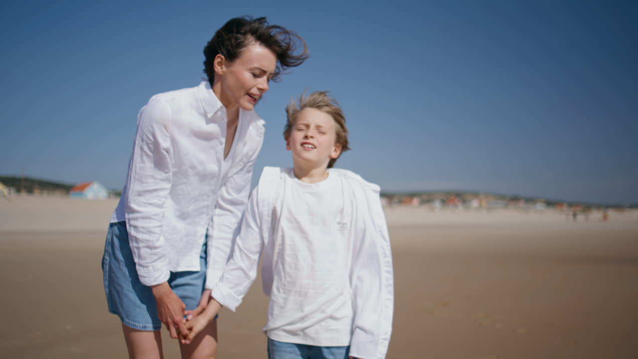 Donna in piedi sulla riva del mare con il figlio che guarda l'orizzonte sull'oceano durante un fine settimana estivo, primo piano