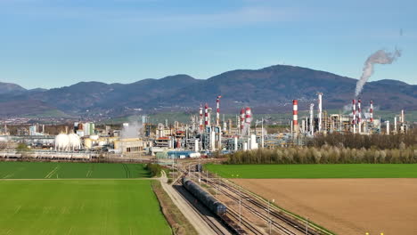 Train-by-a-sprawling-industrial-complex-with-smokestacks,-against-a-clear-sky