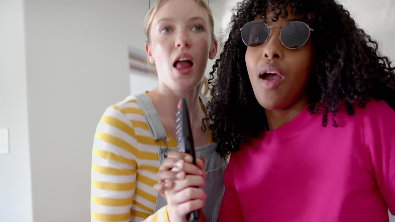 Happy diverse teenage female friends dancing and singing karaoke at home, slow motion