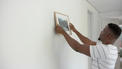 hanging framed picture on wall, man decorating home interior