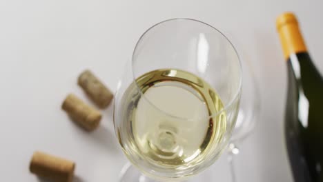 White-wine-bottle,-glasses-and-cork-lying-on-white-surface-with-copy-space