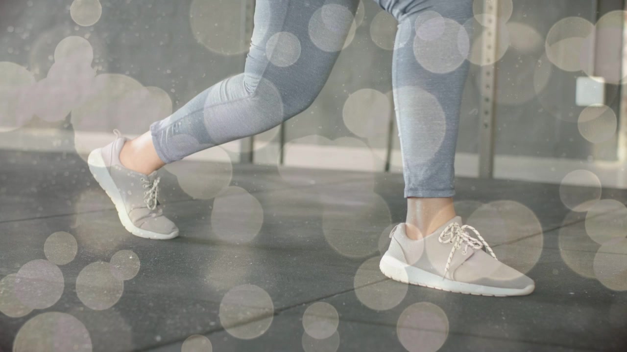 Spor salonunda lunge ve geçişli adımlar yapan, ön ayağını iten kadın. Gücü vurgulamak için ayakkabıları öne çıkaran bokeh efekti.